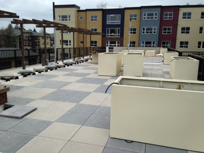 A rooftop patio with light beige planters and gray and light gray square tiles.