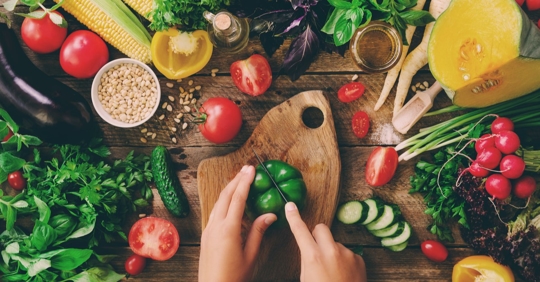 Hands are slicing a green bell pepper on a wooden cutting board.