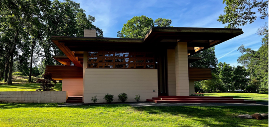 A light beige house with a brown roof, a modern design, sits on a grassy lawn.